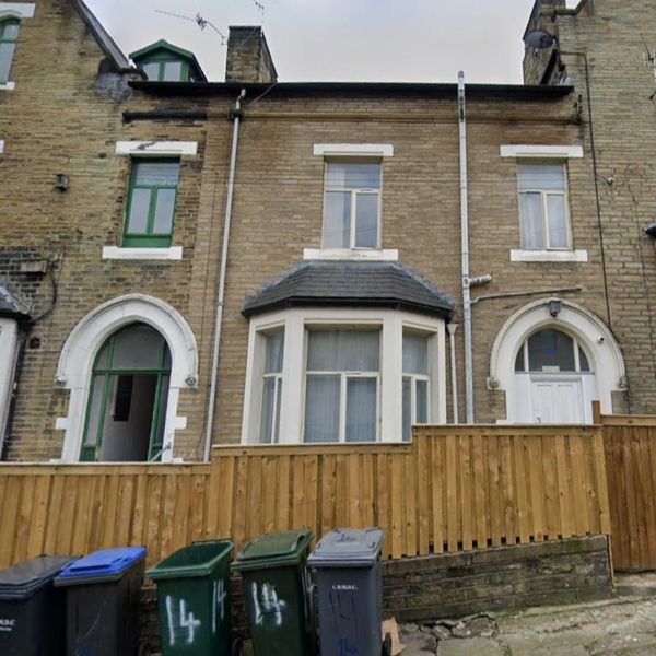 Row of brick houses with green and white doors behind a wooden fence and bins.