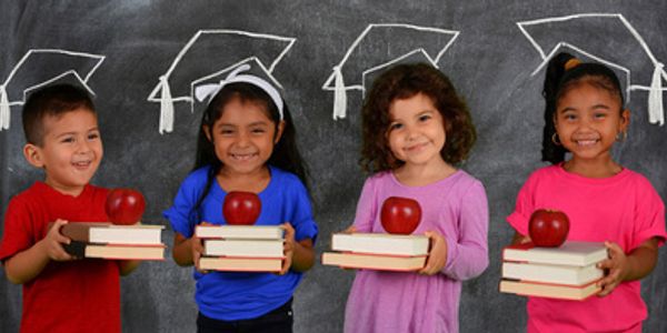 	“Kids smiling while holding books and apples, with a chalk graduation hat drawn on the chalkboard 
