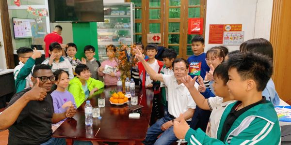 Group of children and adults showing thumbs up around a table with oranges.