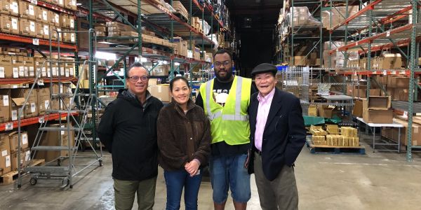 Four people standing in a warehouse aisle.