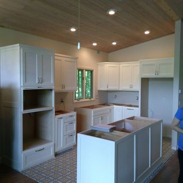New white kitchen cabinets installed with wooden ceiling and patterned floor.