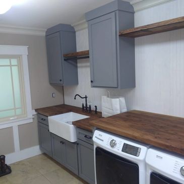Modern laundry room with gray cabinets, farmhouse sink, and wooden countertops.