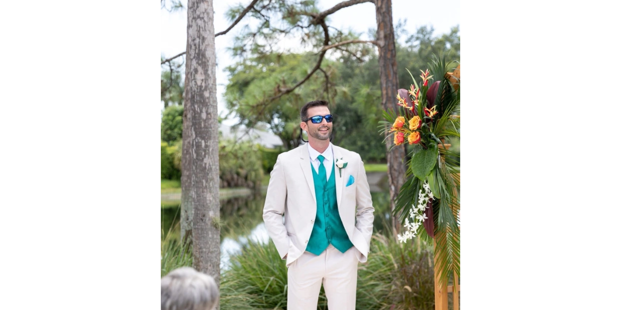 Man in white suit with teal vest and sunglasses at outdoor event.