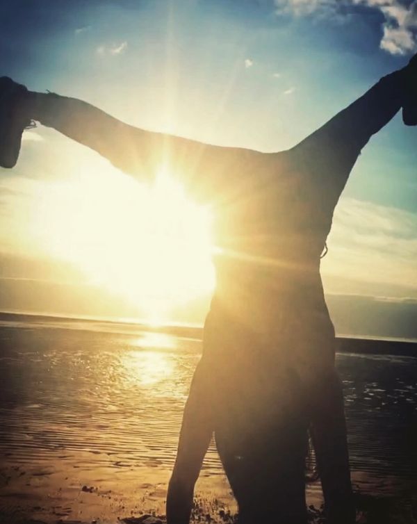 Person doing a handstand on the beach at sunset with sun flare.