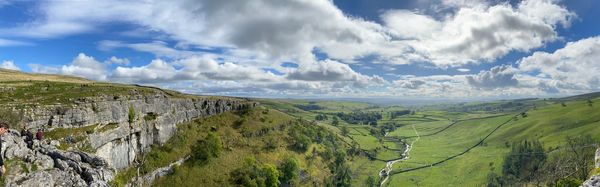 Expansive green valley with rocky cliffs under a partly cloudy blue sky.