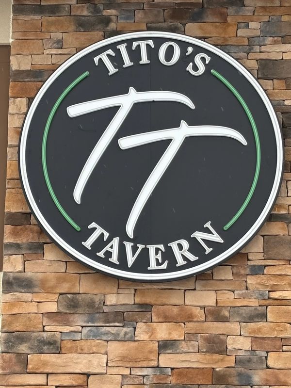 Sign for Tito's Tavern on a stone wall.