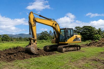 Yellow excavator digging soil in a field under blue sky.
