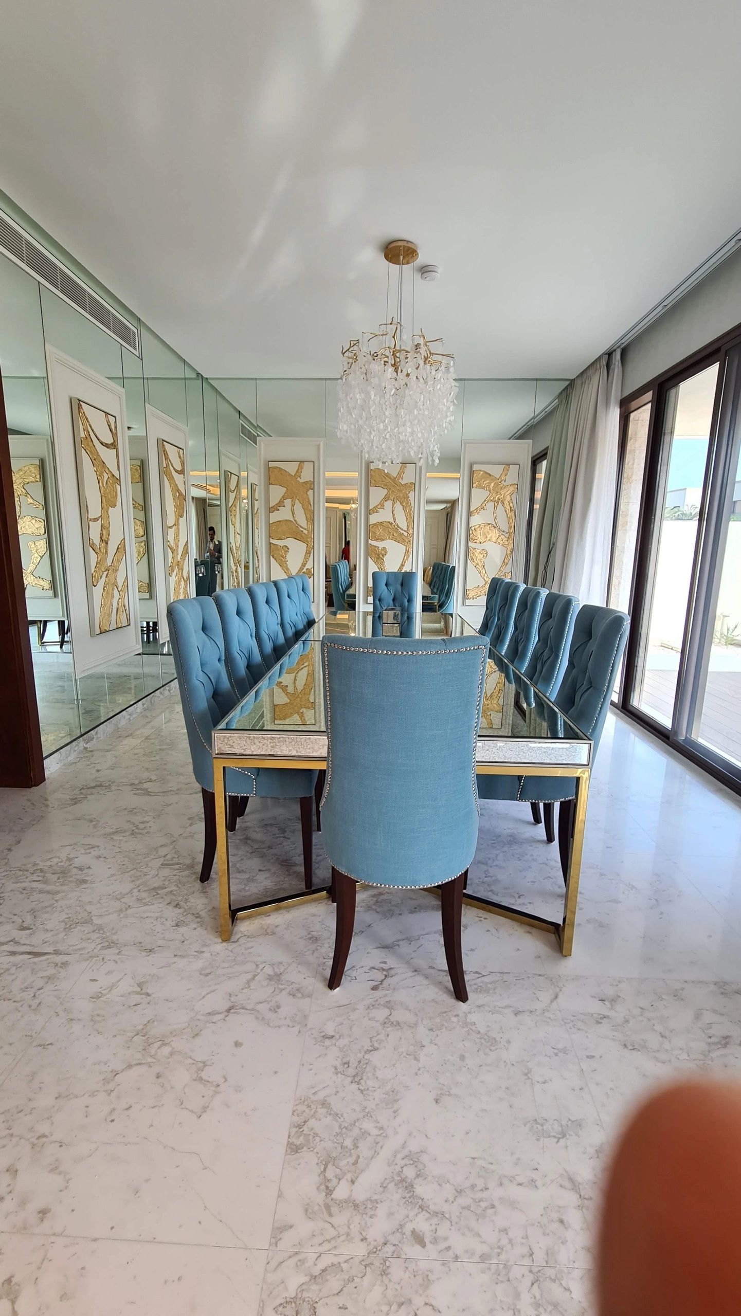 Modern dining room with blue chairs, glass table, and elegant chandelier.