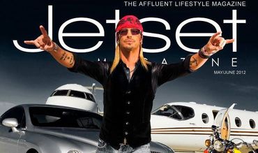 Man in sunglasses and bandana posing in front of luxury private jet and car.