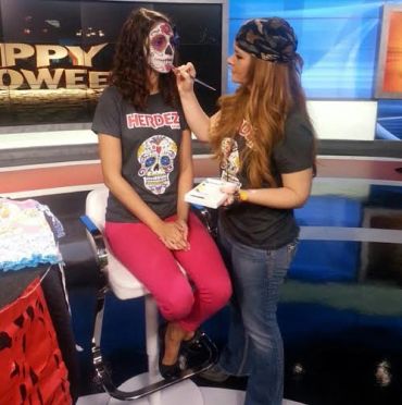Woman painting sugar skull makeup on another woman for Halloween.