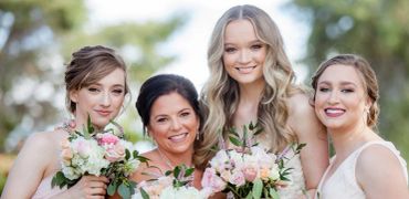 Four women holding bouquets and smiling outdoors.