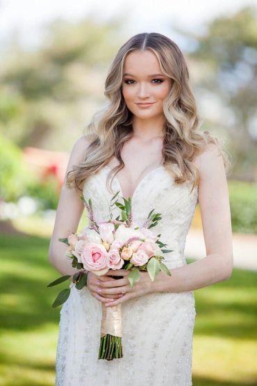 Bride in white dress holding a floral bouquet outdoors.