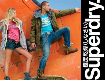 Two models pose against an orange wall with Superdry branding.