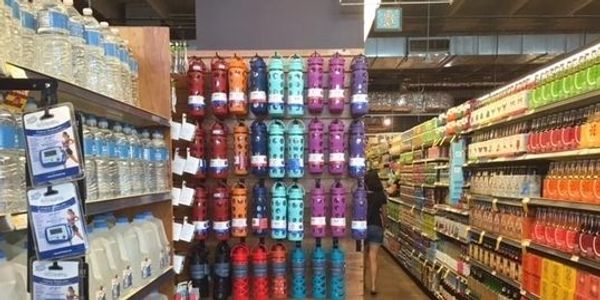 Supermarket aisle with water bottles and colorful water containers.