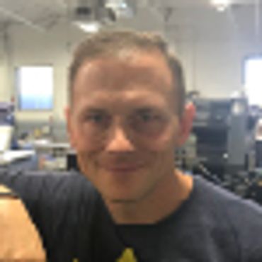 Man smiling indoors, wearing glasses and a dark shirt.