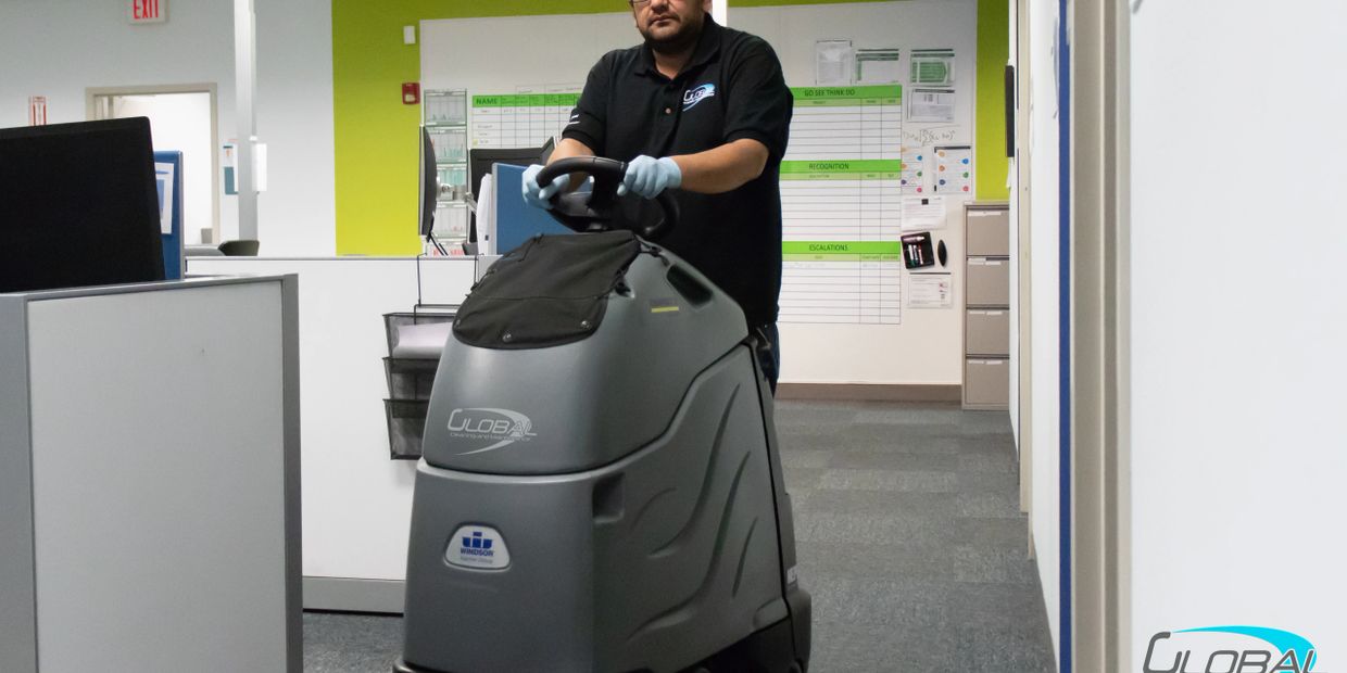 A man using a floor cleaning machine in an office.