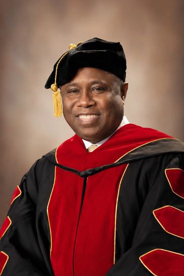 Smiling man in academic regalia with black and red gown.