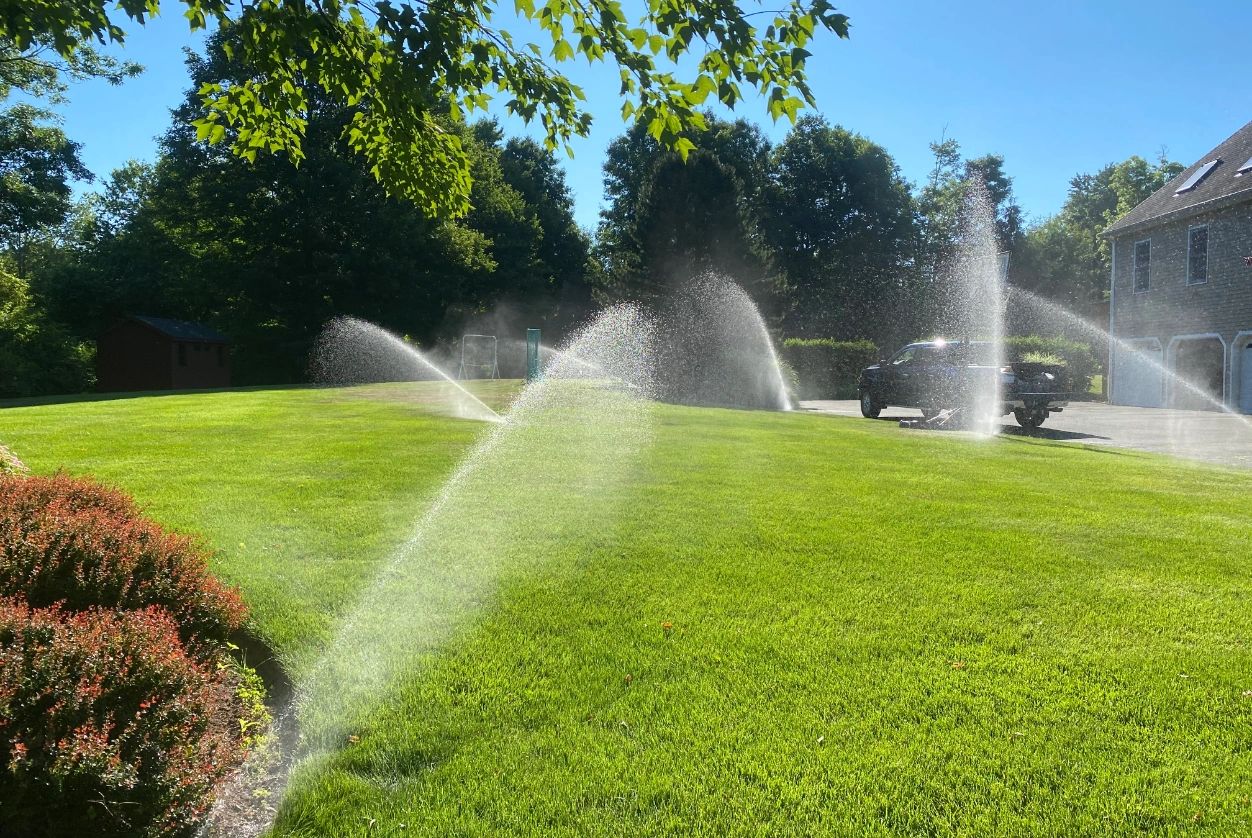 Lawn sprinklers watering green grass with water spray in the garden.