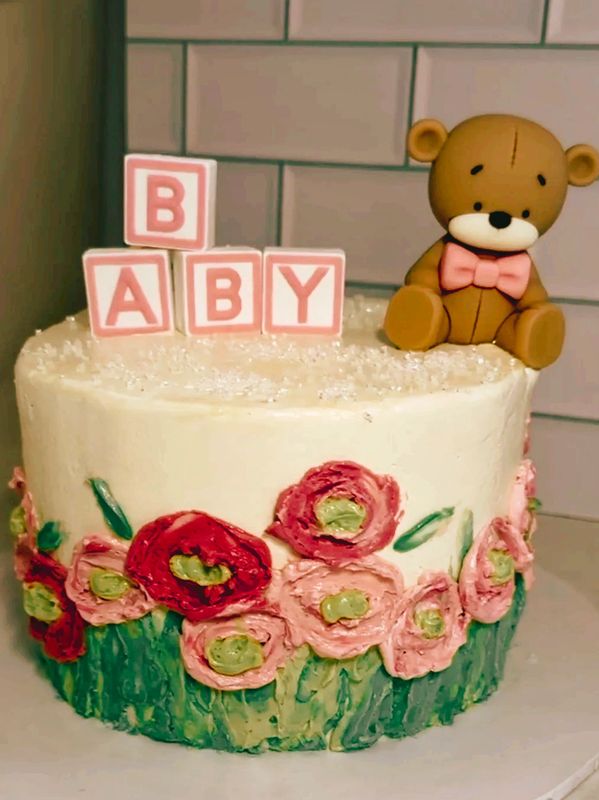 Baby shower cake decorated with floral icing and a teddy bear topper.