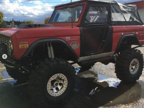 Red and black lifted Ford Bronco with large off-road tires.