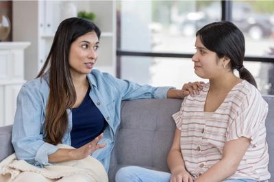 Two women having a serious conversation on a couch indoors.