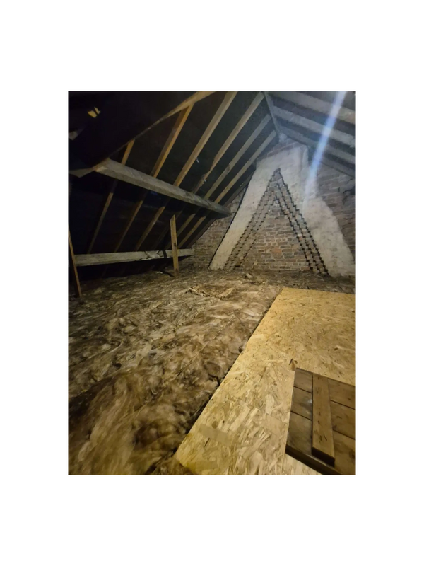 Insulated attic with exposed beams and brick wall.
