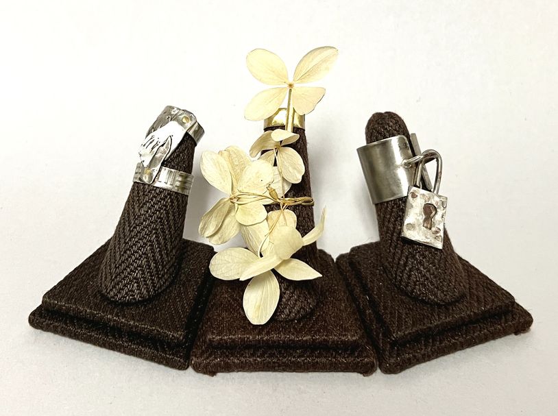 Silver rings with unique designs displayed on brown fabric stands.