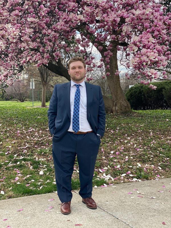 Britton standing in front of a cherry blossom tree wearing a blue suit and tie 