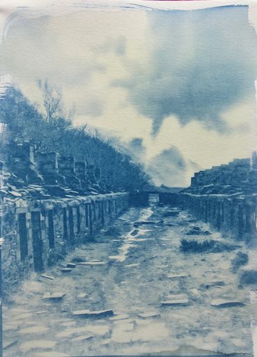Ancient stone pathway flanked by ruins under a cloudy sky.