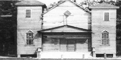 Black and white image of an old wooden church with two towers and a centered entrance.