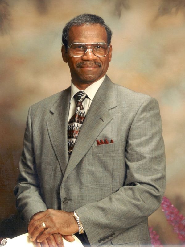 Man in a gray suit with glasses posing confidently against a soft background.