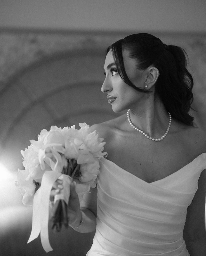Bride in elegant dress holding bouquet, looking sideways.