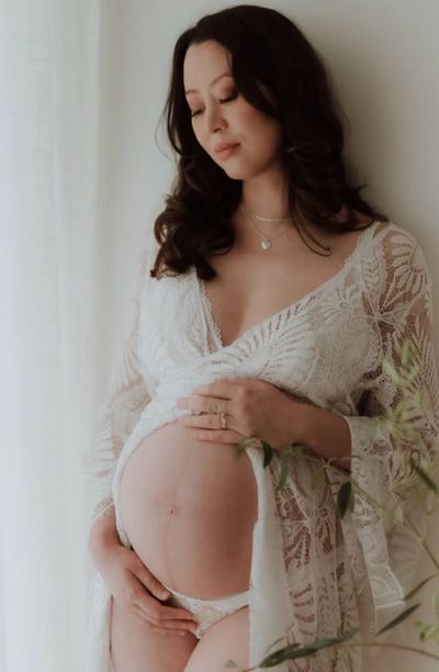 Pregnant woman in delicate white lace robe gently cradling her belly.