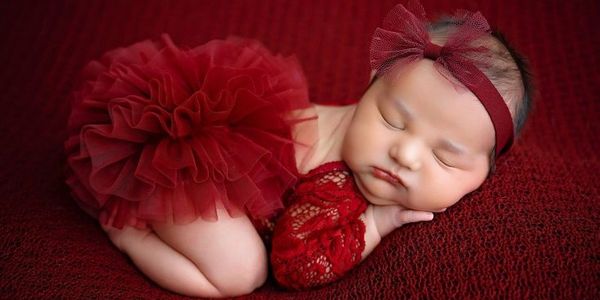Sleeping baby girl in red outfit and headband on matching red blanket.