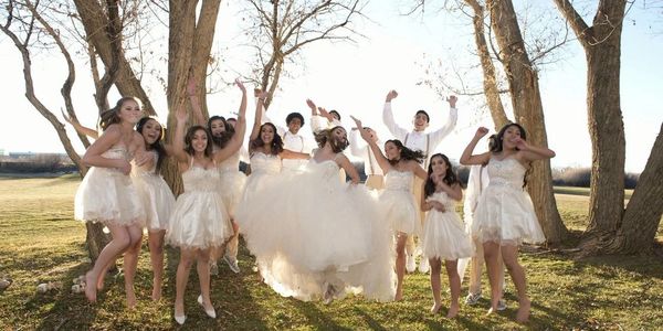 Group of young women and men in white dresses and shirts celebrating outdoors.