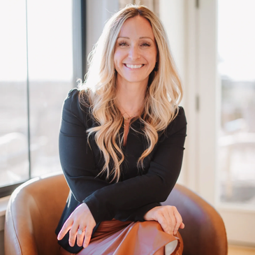 Smiling woman with long blonde hair seated indoors.