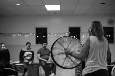 Carol Edwards is holding a frame drum and leading a drum circle in a demonstration. 