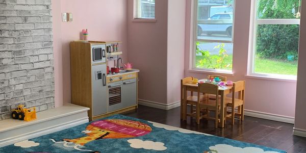 Cozy children's playroom with toy kitchen, table, and colorful rug.