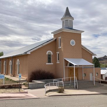 A historic beige church with a white steeple under a cloudy sky.