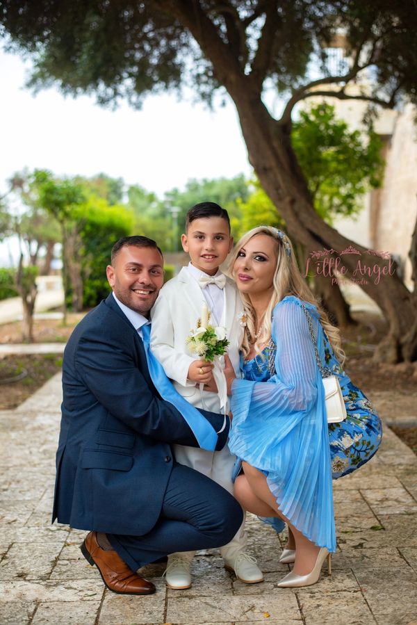 A happy family dressed elegantly, posing outdoors with greenery in the background.