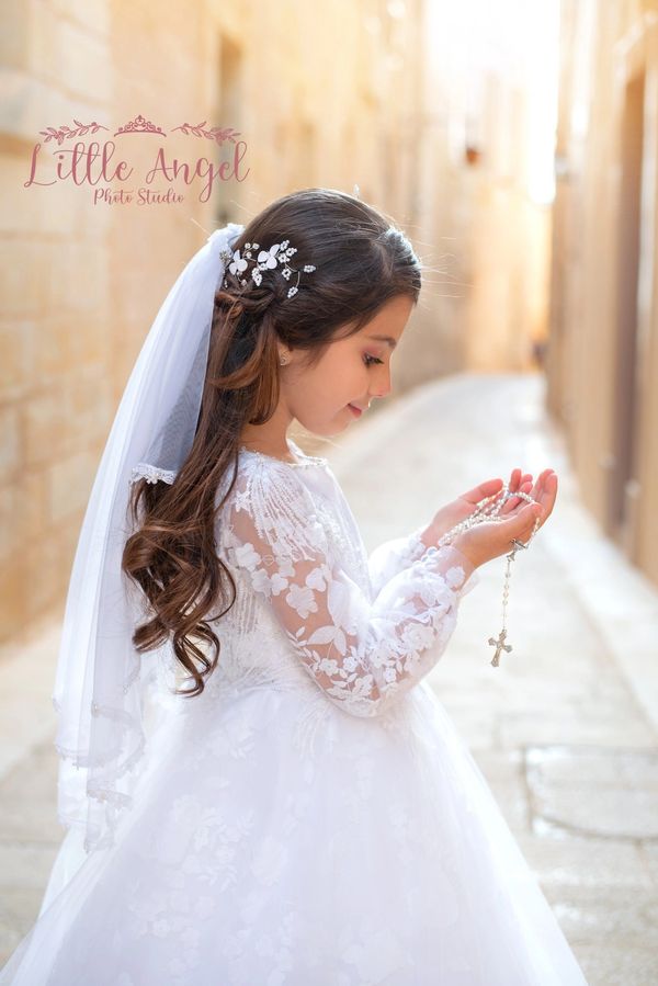 Young girl in white dress holding rosary beads in prayer.