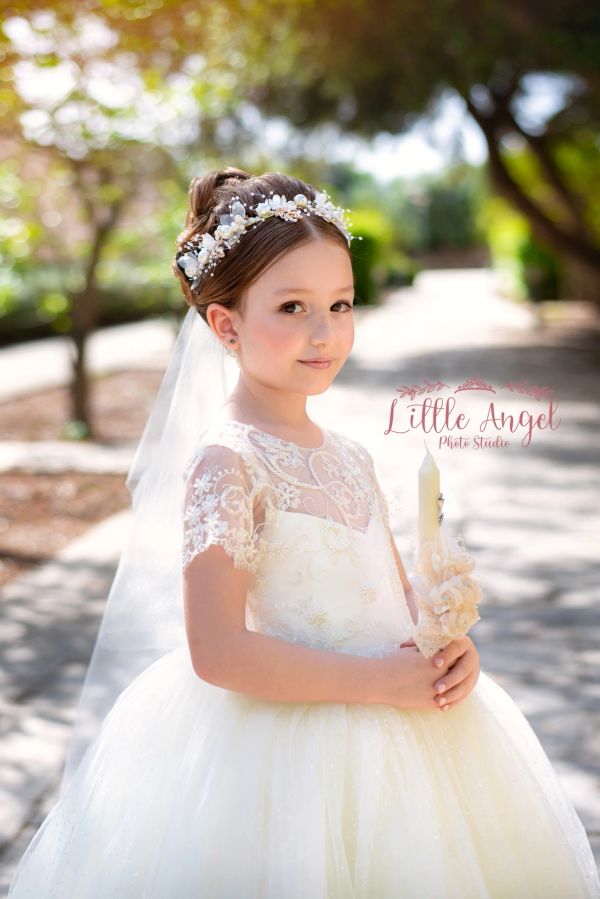 Young girl in a white lace dress holding a decorated candle outdoors.