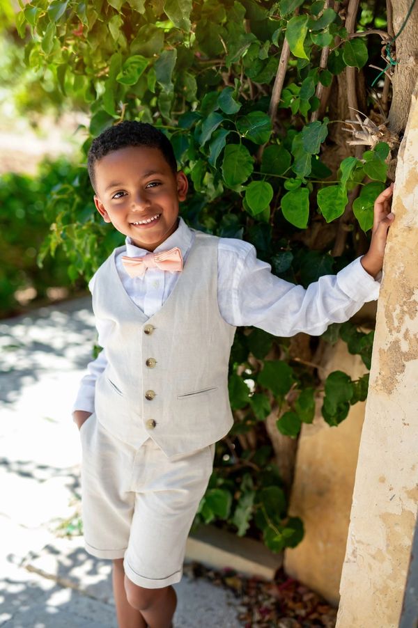Smiling boy in a light beige vest and shorts with a peach bow tie.