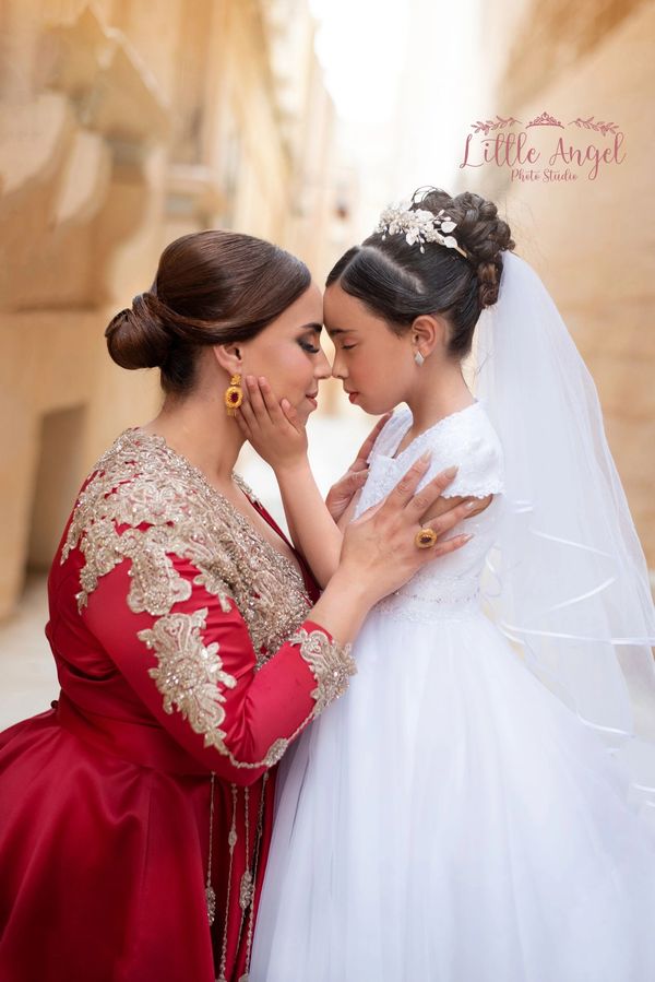 Tender moment between woman in red dress and girl in white dress with veil.