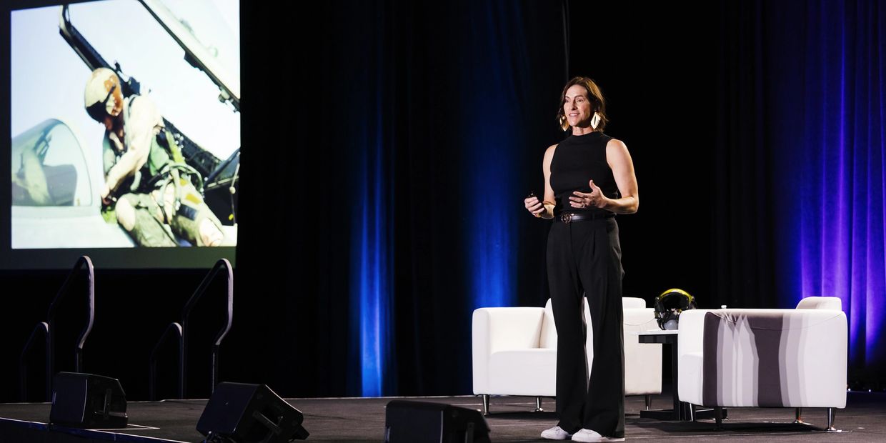 Woman speaking on stage with military presentation.
