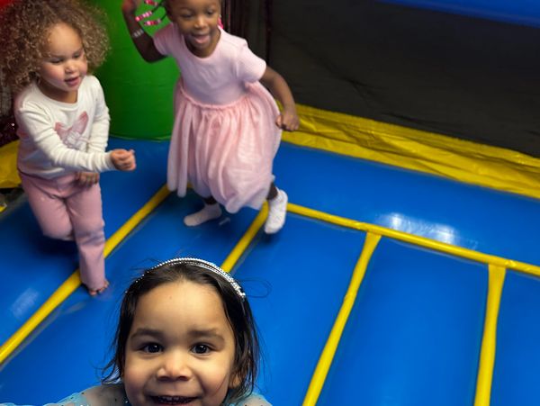 Three young girls playing and smiling on a colorful inflatable surface.