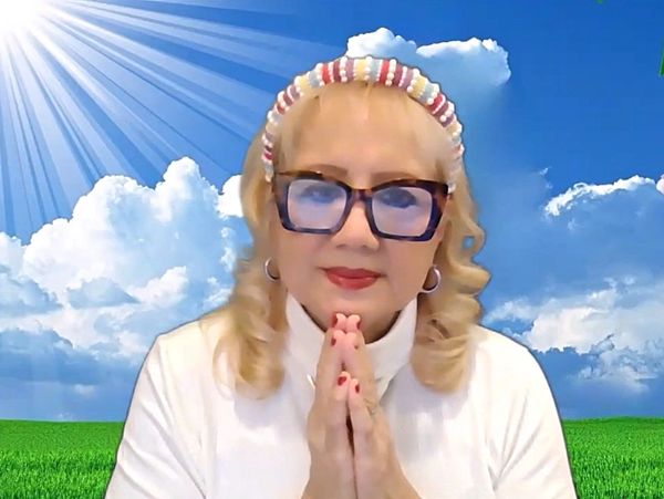 Woman with glasses and colorful headband praying outdoors under the sun.