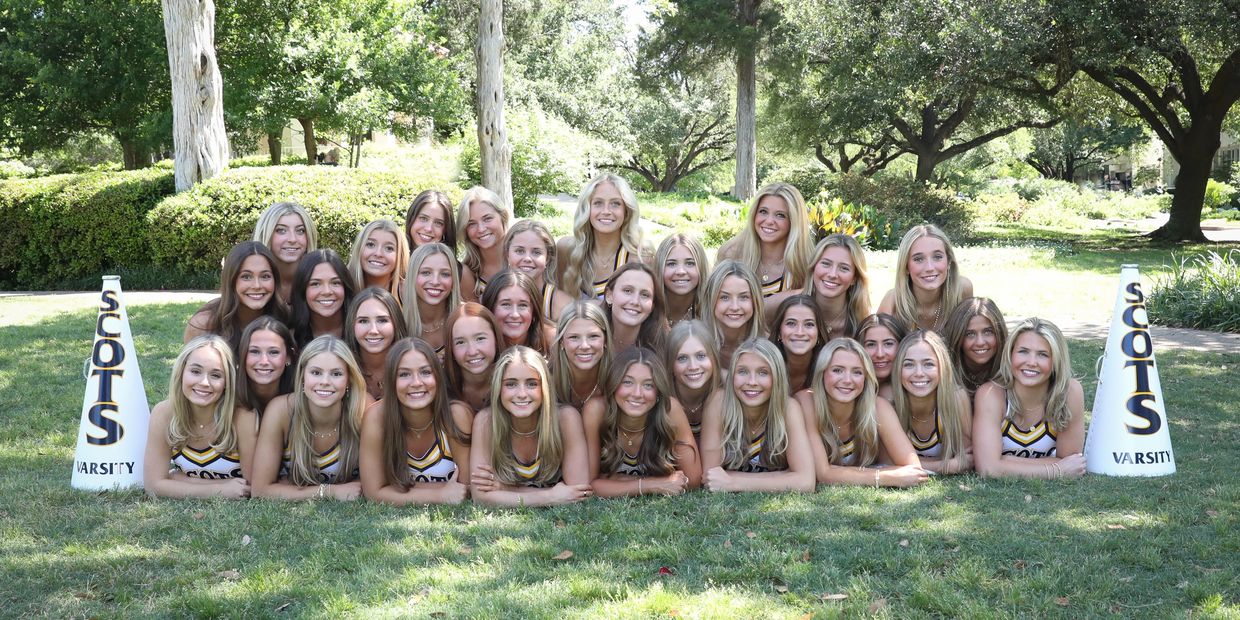 Cheerleading team posing outdoors on grass with megaphones.