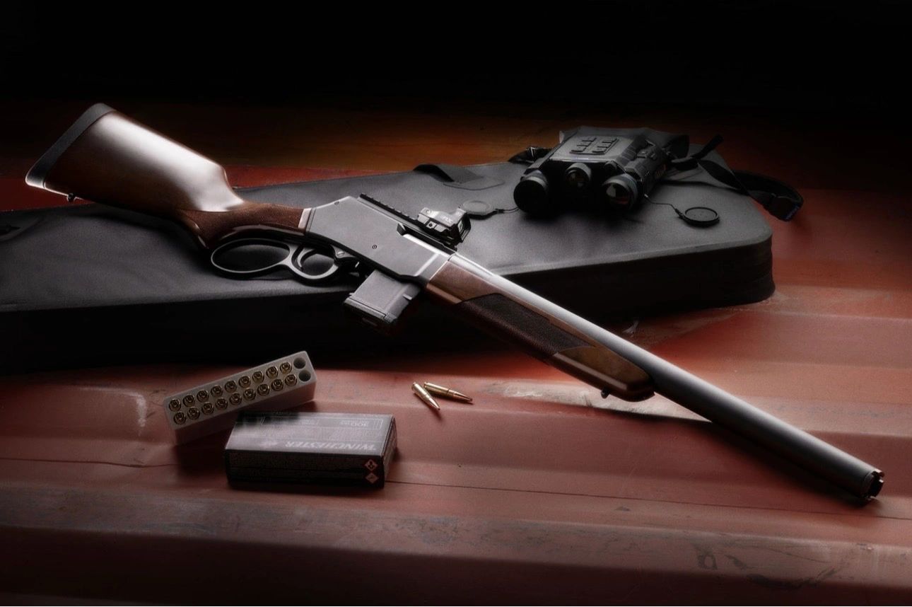 A hunting rifle with ammunition and binoculars on a table.
