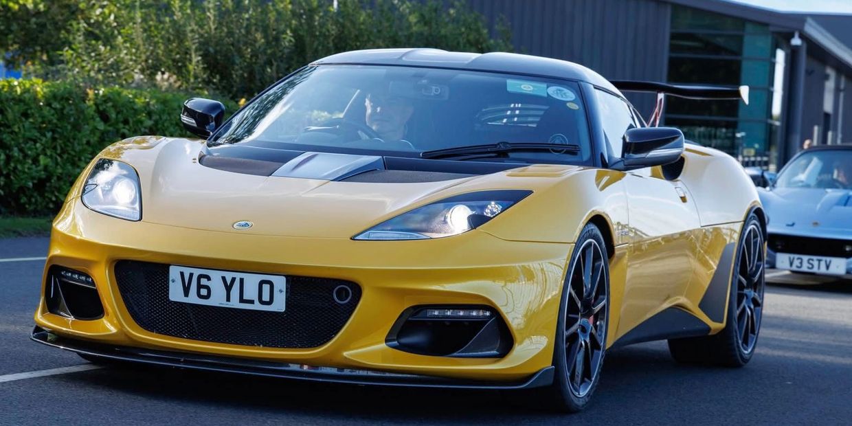 Yellow Lotus sports car driving on a road with a white car behind it.
